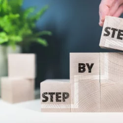 Une personne qui empile des cubes en bois pour écrire "step by step".